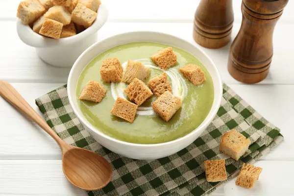 Tasty broccoli cream soup with croutons served on white wooden table, closeup