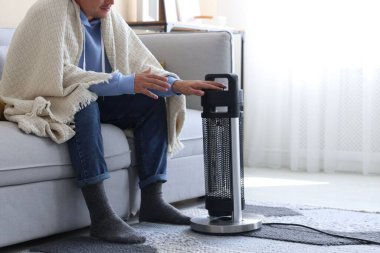 Evinde elektrikli ısıtıcının yanındaki battaniyeli genç adam, yakın çekim.