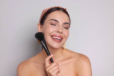 Açık gri arkaplanda makyaj fırçası olan güzel bir kadın.