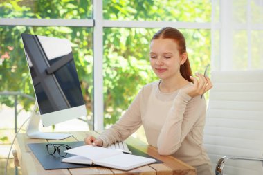 Kapalı alandaki ahşap masada bilgisayarla kitap okuyan genç bir kız. Ev işyeri