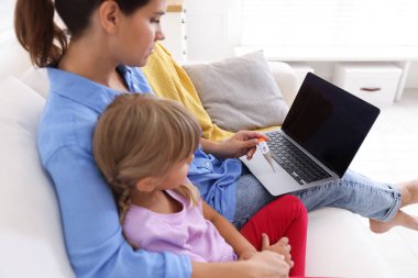 Sağlığınıza. Anne ve hasta kızı evdeki kanepede dizüstü bilgisayarla doktorla görüşüyorlar.