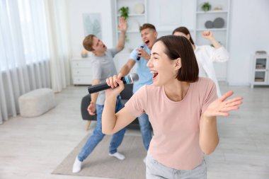 Genç bir kadın evde arkadaşlarıyla karaoke yapıyor, seçici odaklı.