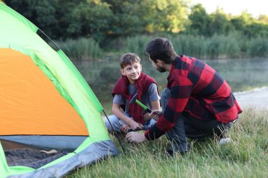 Baba ve oğul nehir kenarında kamp çadırı kuruyorlar.