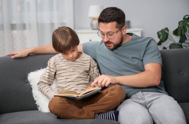 Baba ve oğul evdeki kanepede kitap okuyorlar.