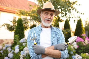 Portrait of elderly man in hat with gardening tools outdoors
