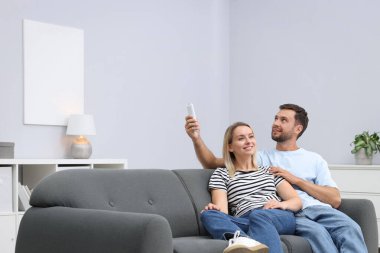 Evdeki kanepede klima kontrol etmek için uzaktan kumanda kullanan çift. Metin için boşluk