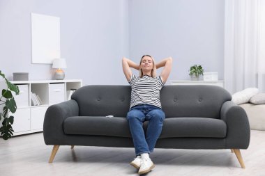 Evdeki koltukta klimalı uzaktan kumandalı bir kadın.