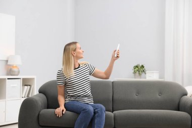 Evdeki koltukta uzaktan kumandayla klima kullanan bir kadın.