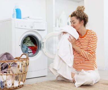 Çamaşır makinesinin yanında çamaşırları olan mutlu kadın.