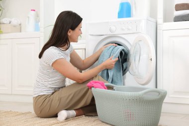 Çamaşır makinesinden çamaşırları çıkaran kadın.