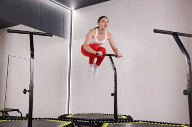 Spor salonunda trambolinde zıplayan genç bir kadın. Düşük açılı.