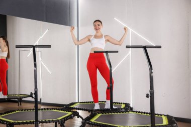 Gülümseyen kadın spor salonundaki mini egzersiz trambolininde kaslarını gösteriyor.