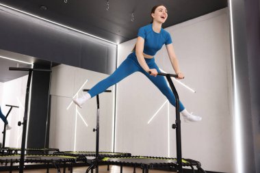 Jimnastik stüdyosunda trambolinde zıplayan mutlu bir kadın.