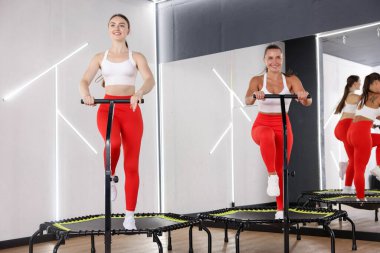 Gülümseyen kadınlar spor salonundaki trambolinlerde antrenman yapıyorlar, düşük açılı.