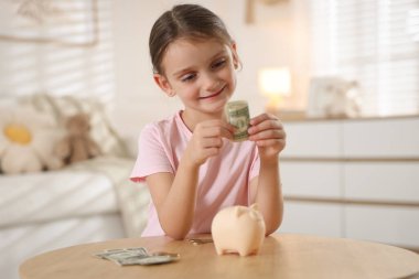 Küçük kız cep harçlığı ve domuz kumbarası ile ahşap masada.