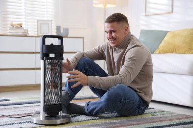 Evdeki elektrikli ısıtıcının yanındaki genç adam.