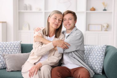 Mutlu oğul ve annesi evde kanepede kucaklaşıyorlar.