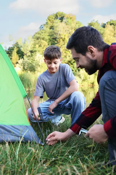 Baba ve oğul dışarıda kamp çadırı kuruyorlar.