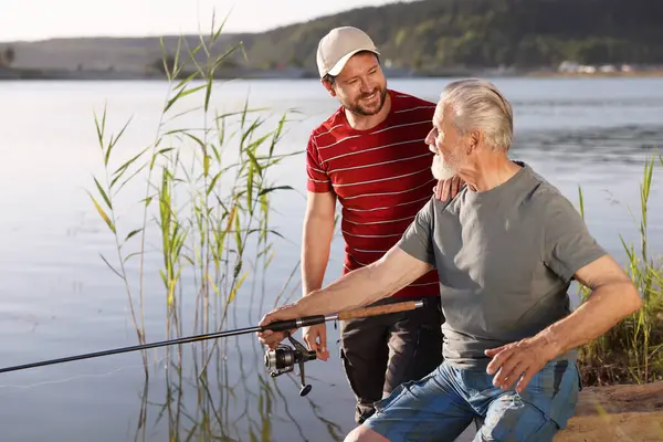 Yaşlı babası ve mutlu oğlu birlikte nehir kenarında balık tutuyorlar.