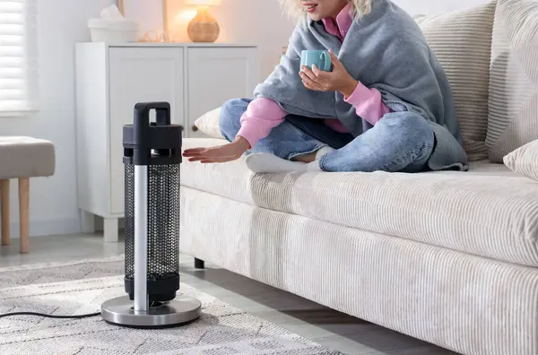 Evinde elektrikli ısıtıcının yanında içki içen genç bir kadın, yakın çekim.