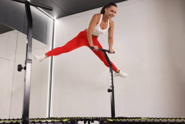 Spor salonunda trambolinde zıplayan gülümseyen kadın, düşük açı.