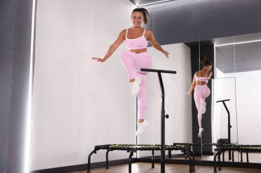 Spor salonundaki aynanın yanında trambolinde zıplayan gülümseyen kadın, düşük açılı görüş.