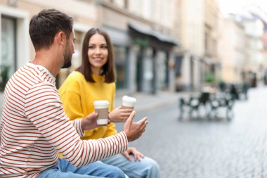 Paket kahve. Şehir caddesinde kağıt bardakta içki içen çift, seçici odaklı. Metin için boşluk