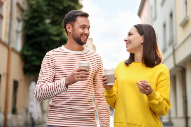 Paket kahve. Kağıt bardaklı bir çift şehir caddesinde yürüyor, düşük açılı.