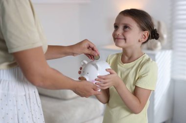 Anne ve kızı evdeki domuz kumbarasına cep harçlığı yatırıyor.