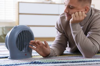 Evdeki elektrikli ısıtıcının yanındaki genç adam.