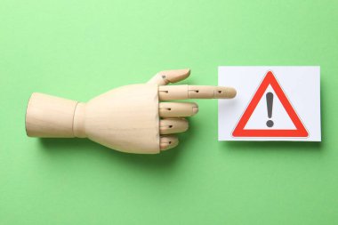 Risk. Yeşil zemin üzerinde uyarı işareti olan kağıt parçasına bakan manken eli düz yatıyordu.