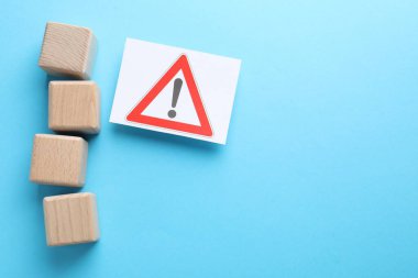 Açık mavi zemin üzerinde uyarı işareti olan boş küpler ve bir sayfa kağıt. Metin için boşluk