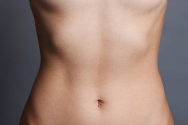 Gri arka planda düz göbekli genç kadın, yakın plan.