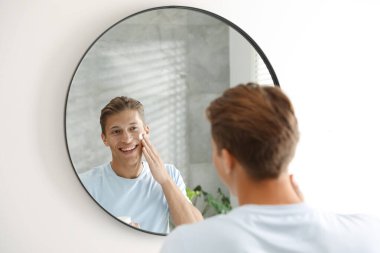 Yakışıklı genç adam evde aynanın yanında yüzüne krem sürüyor.