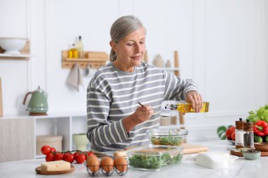 Üst düzey kadın mutfaktaki beyaz mermer masada salata pişiriyor.