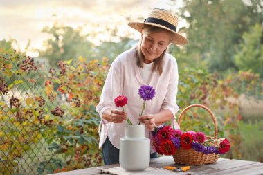 Yaşlı kadın bahçedeki ahşap masada güzel çiçekler yapıyor.