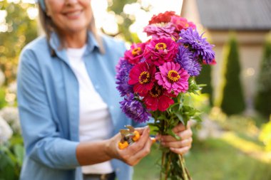 Bahçesinde budama ve çiçek demeti olan son sınıf öğrencisi kadın, yakın plan.