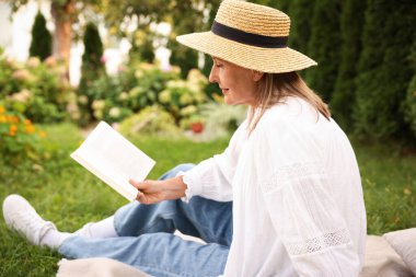 Bahçe battaniyesinde kitap okuyan son sınıf öğrencisi kadın.