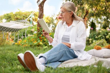 Bahçe battaniyesinde kitap okuyan son sınıf öğrencisi kadın.