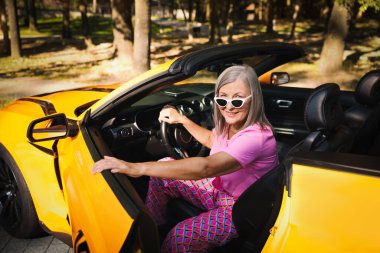 Güneş gözlüklü şık bir son sınıf öğrencisi modern Cabriolet 'ten dışarı çıkıyor.