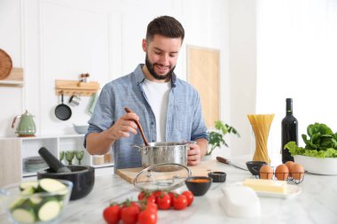 Mutfaktaki masada yemek pişiren gülümseyen adam.