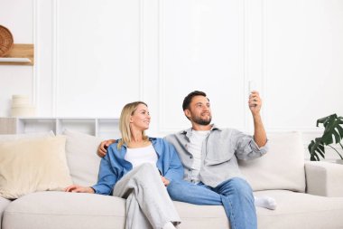 Evdeki koltukta uzaktan kumandayla klima kullanan çift.