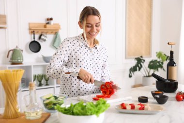 Yemek pişirme süreci. Mutfakta masada biber kesen gülümseyen kadın.