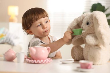 Oyuncak tavşancığıyla evde çay partisi yapan şirin bir çocuk.