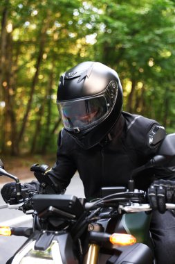 Kasklı genç adam modern motosikleti açık havada kullanıyor.