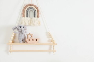 Shelf with soft toy elephant and wooden boat on white wall. Space for text