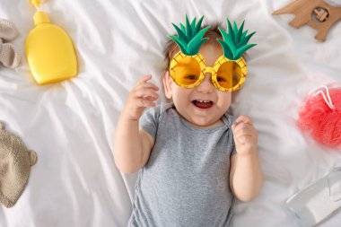 Yatağında güneş gözlüğü ve aksesuarları olan sevimli bir bebek.