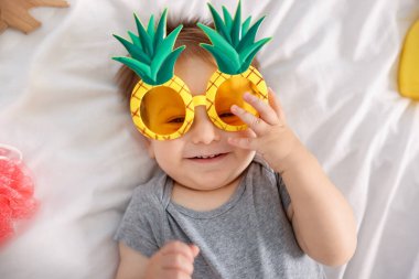 Yatağında güneş gözlüğü ve aksesuarları olan sevimli bir bebek.