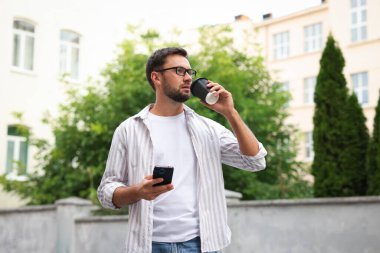 Paket kahve. Elinde kağıt bardak içki ve akıllı telefon olan bir adam.