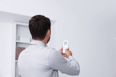 Ofisteki klimayı kontrol etmek için uzaktan kumanda kullanan bir adam.